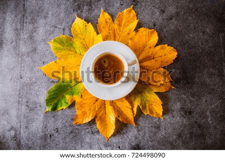 The cup of coffee with yellow autumn leaves on a concrete background