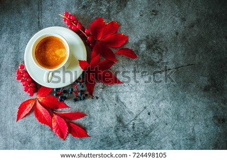 The cup of coffee with red autumn leaves on a concrete background
