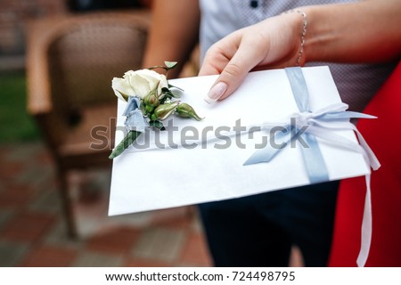 White wedding envelope with a boutonniere in the hand of a woman. A gift from the invited guests to the wedding.  Royalty-Free Stock Photo #724498795