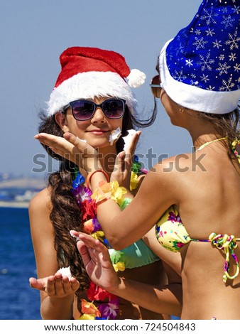 Photo of two young girls in Santa's hats having fun on the beach with shaving foam. Happy Christmas on vacation