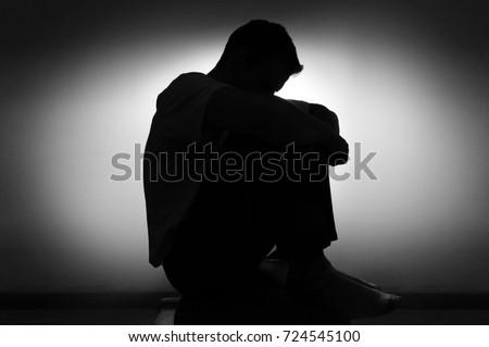 sad silhouette of a man in depression sitting on a chair with his head down Royalty-Free Stock Photo #724545100
