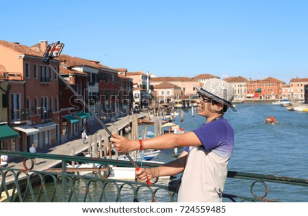 cute boy with glasses and hat makes a selfie with the smartphone on the bridge of the island of Murano near Venice in Italy