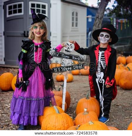 Trick or treat. Boy in a Halloween costume of skeleton with hat and smocking and girl with witch costume between orange pumpkins. Halloween kids with halloween costumes