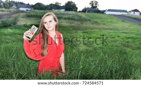 Beautiful girl in red evening dress makes a selfie in nature.