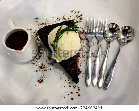 Brownies cake served with ice cream, topped with chocolate on a white plate.