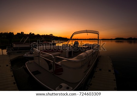 Lake sunset featuring docked pontoon boat Royalty-Free Stock Photo #724603309