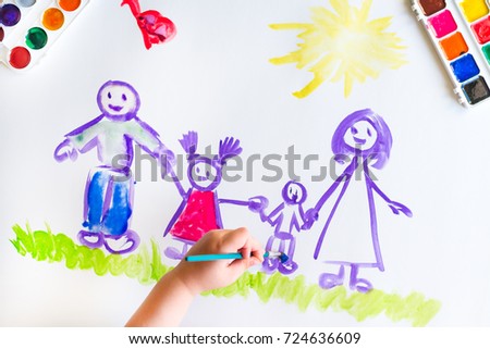 The top view of the child's hand paints a sketch of the family with brush of watercolor on a white sheet of paper