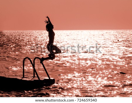 Silhouette of a girl against the sky jumping in the sea on the sunset, concept of happiness