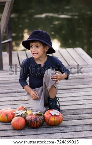 Positive boy sitting with pumpkins on the river bank