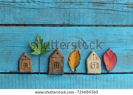autumn background /  the figures of houses and birds made of dough with autumn leaves on blue wooden background