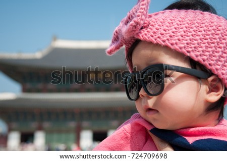A shot of mother is holding a cute baby girl with pink jacket, pink headband and black sunglasses in Gyeongbokgung Palace. Focus at infant girl.