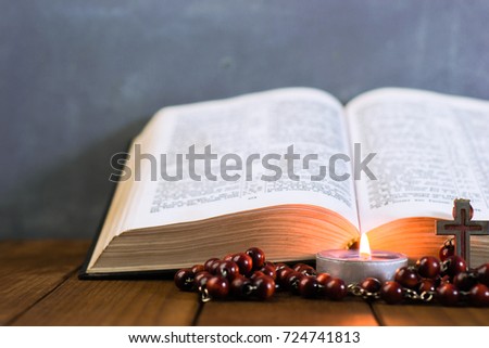 Bible crucifix and beads with a candle on a brown wooden table. Beautiful background.Religion concept.