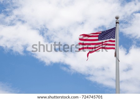Weathered American flag on a pole with blue sky background. Old flag, flapping in the wind on pole. Fourth of July, Patriotism. Worn out American flag. July 4th