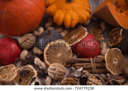 Autumn picture. Texture of spilled pumpkins, walnuts, peanuts, pomegranates, cinnamon sticks, dry orange slices, whole fig fruits and anise stars at natural wooden background