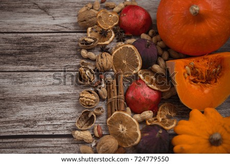 Autumn picture. Texture of spilled pumpkins, walnuts, peanuts, pomegranates, cinnamon sticks, dry orange slices, whole fig fruits and anise stars at natural wooden background