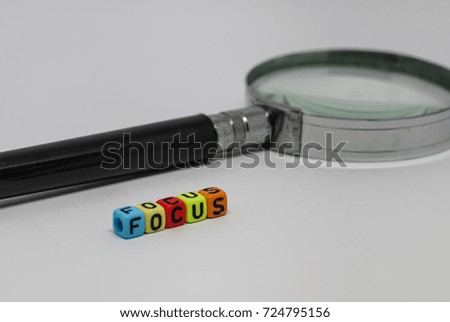 Conceptual image of focus required in business on white background. "FOCUS" spelled in colorful beads in focus. Magnifying glass and others in gradient bur. White background.