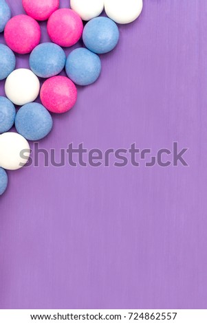 Top view of upper left corner frame of colored chocolate coated candy on wooden purple background. Copy space