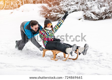 Young happy couple having fun on snowy day, sledding and smiling together