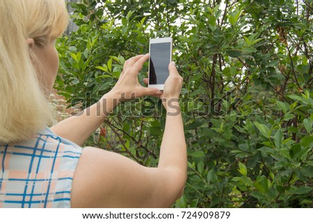 Blonde woman uses a smartphone to take a selfie in the Park in the summer.