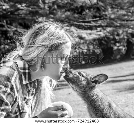 Young blonde woman is kissing Kangaroo in a park. People interacting with kangaroo at zoo. Black and white. Square format. France