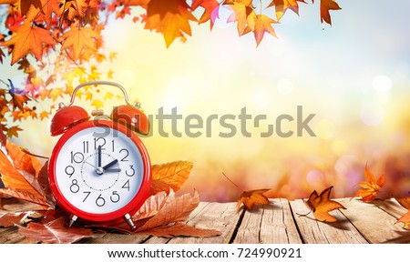 Daylight Savings Time Concept - Clock And Leaves On Wooden Table Royalty-Free Stock Photo #724990921