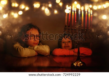 Low key image of jewish holiday Hanukkah background with two cute kids looking at menorah (traditional candelabra) and burning candles.