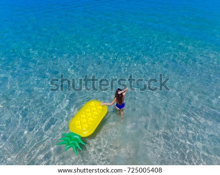 Top aerial view of a woman with inflatable mattress in a pineapple shape going to swim. On holidays having fun and relaxing at the beach.