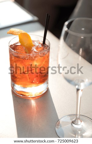 Old fashion cocktail with orange peel garnish in a traditional glass, in bright sunlight at an outdoor restaurants and bar, beside empty wine glass