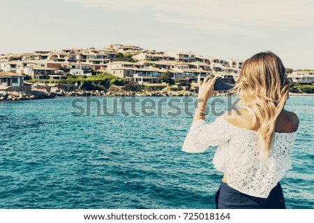 Tourist woman taking photos of the sea and small italian city on her cell phone, selective focus