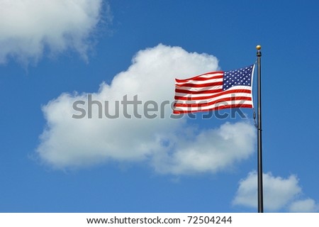 The American Flag Flying Against A Blue Sky With White Clouds On A Windy Day