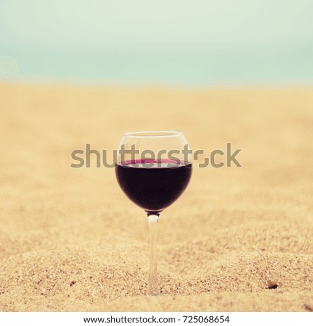 A glass of red wine on the sand at the sea coast. Vacation pleasure concept