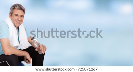 Portrait Of Smiling Fitness Man Holding Water Bottle Against Blue Sky