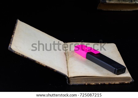Old book lying on a black countertop and office marker. black background