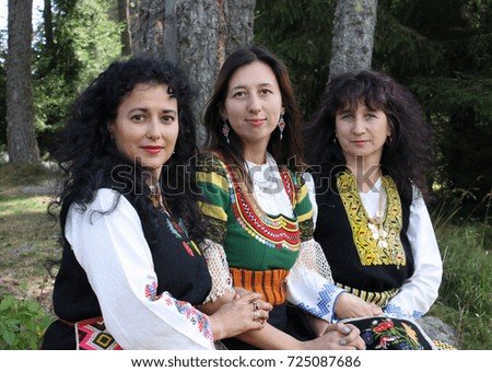 Three beautiful women in traditional Bulgarian folklore costumes in an outdoor scene