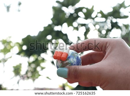 Hand hold miniature world globe with capsules in blur natural tree and bright light background