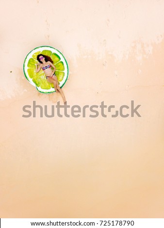 Top aerial view of a woman in a bikini lying and sunbathing on a round beach towel in the form of lime.