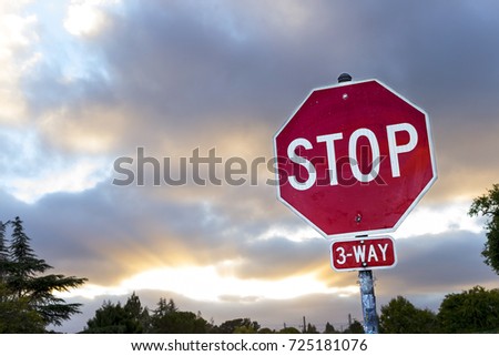 A weathered stop sign with clouds and rays of sunlight in the background.