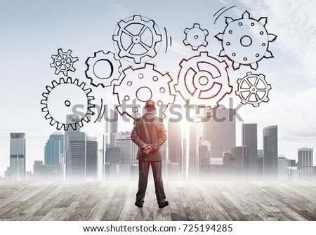 Back view of businessman looking at modern city and drawn gear mechanism