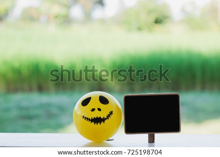 Self Made Hand Drawn Smiley Face Halloween Pumpkin Ball in Yellow at the balcony with blank black signboard and green field background - Vintage Filter
