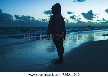 Silhouette photo of a little girl standing on the ocean coast in dark