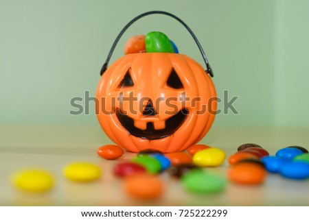 Happy Halloween,colorful of milk chocolate candy in bowl, orange plastic pumpkin filled with candies, trick or treat with seasonal sweet toffee on wooden table