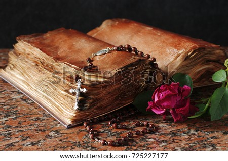 The Bible, a crucifix, a dry rose on a granite table
