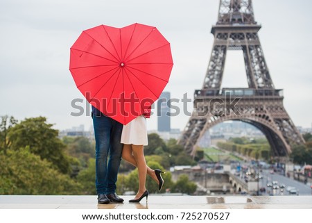 The couple hidden with red umbrella in front of the Eiffel tower in Paris