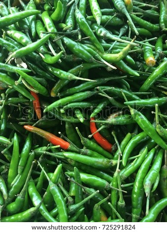 Many green chilies piled on top of each other with some red chilies