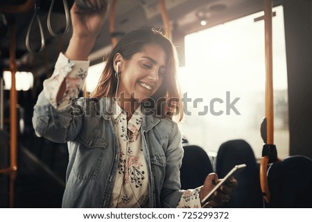 Young woman smiling while standing by herself on a bus listening to music on a smartphone  Royalty-Free Stock Photo #725299372