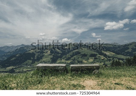 Scenery moody alpine panorama of Switzerland in sunny day with view on mountains, green forest, meadow, blue sky and white clouds and with a bench for rest in the foreground
