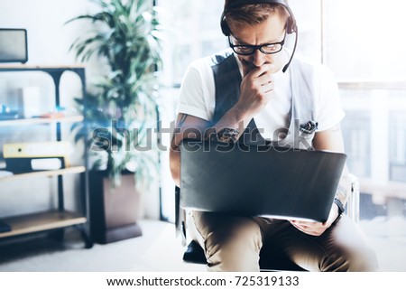 Businessman working at modern office on his digital tablet holding in hands.Cute young man wearing audio headset and making video conversation via digital tablet.Blurred background
