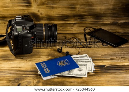 Traveling concept with blank smart phone, headphones, ukrainian passport, dollars and photo camera on wooden desk. Mock up