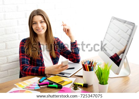 Creative designer with phone while using laptop in office