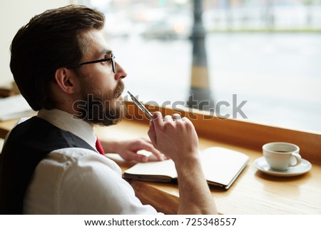 Posh young man with pen thinking of ideas while making notes in notebook Royalty-Free Stock Photo #725348557